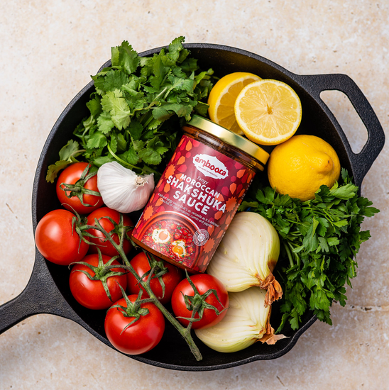Amboora Moroccan Tagine Sauce in a jar in a pan surround with ingredients