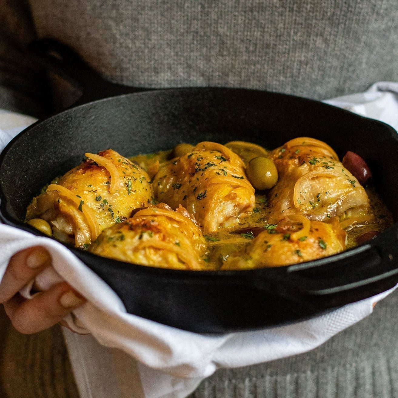 Amboora Moroccan Tagine Sauce in a jar with a cooked chicken tagine paired with olives carried by a person