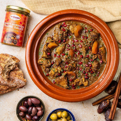 Amboora Moroccan Tagine Sauce in a jar with a cooked meat tagine paired with apricots and pomegranate