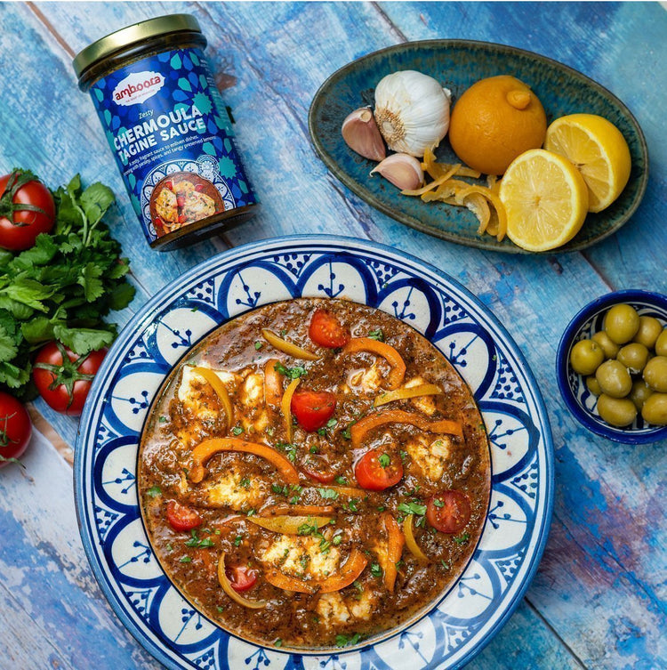 Amboora Moroccan Tagine Cooking Sauce in a jar with a cooked fish tagine paired with tomato and peppers